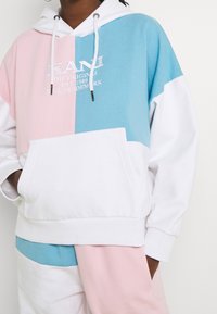 Sudadera con capucha que presenta paneles en rosa, azul y blanco. Tejido suave con un bolsillo frontal, capucha con cordón y detalle del logo bordado.