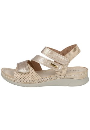 Sandalia beige de punta abierta con parte superior suave perforada, dos tiras ajustables de velcro, detalles con textura metálica y suela blanca acolchada.