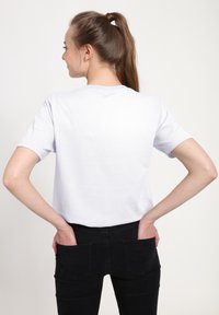 Hvid bomulds t-shirt med rund halsudskæring og korte ærmer, båret med sorte jeans med baglommer, set bagfra.