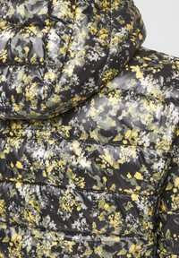 Polstret jakke med et sort, gråt og gult blomstermønster. Har hætte og quiltet tekstur med glat, skinnende materiale.