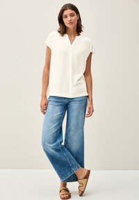 Blouse blanche à manches courtes avec un col en V, associée à un jean bleu clair à jambes larges et des sandales tressées marron. Tissu doux avec un minimum de détails.