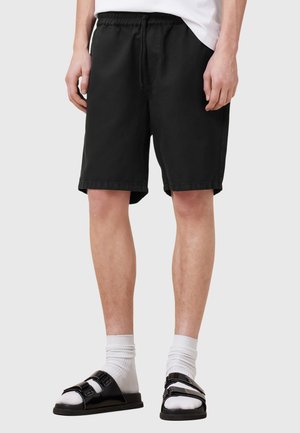 Black cotton shorts with an elastic waistband, side pockets, and a relaxed fit, paired with black sandals and white socks.
