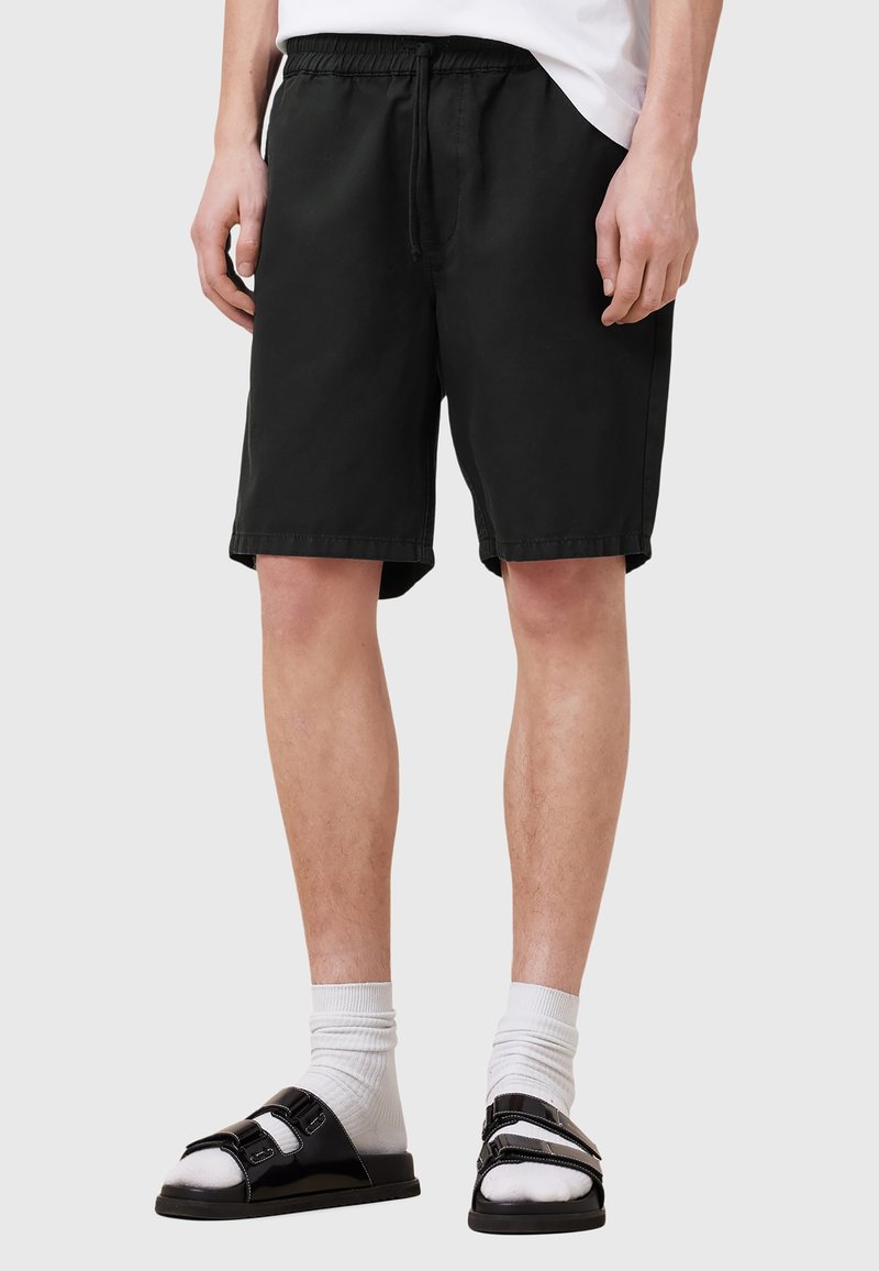 Zwarte katoenen shorts met een elastische tailleband, zijzakken en een relaxed fit, gecombineerd met zwarte sandalen en witte sokken.