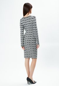 Schwarzes und weißes gemustertes Kleid mit figurbetontem Design, langen Ärmeln und knielangem Saum. Genossen mit schwarzen High Heels.