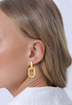 Goldene Metallohrringe mit einem verbundenen ovalen Design, glatter Textur und einer auffälligen, übergroßen Silhouette.