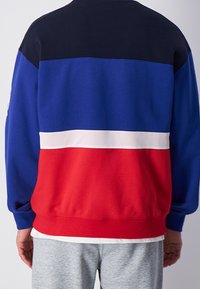 Farbblockiertes Sweatshirt in Blau, Rot und Marineblau. Verfügt über einen weißen Mesh-Streifen in der Mitte und gerippte Bündchen. Weicher Stoff.