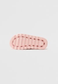 Rosa gummiskosula med en vågig design, som har små cirkulära utskärningar och räfflad textur för grepp.