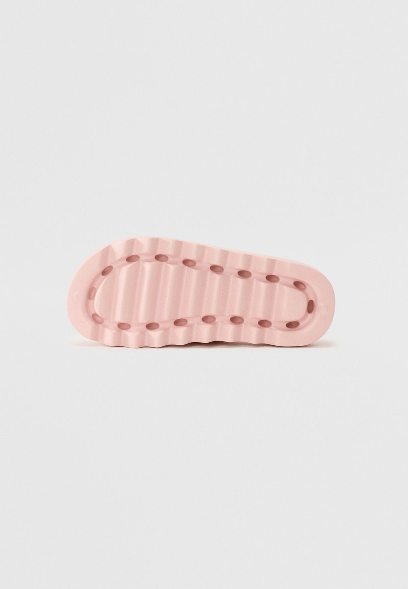Różowa gumowa podeszwa sportowa z falistym wzorem, z małymi okrągłymi wycięciami i żłobioną teksturą dla lepszej przyczepności.