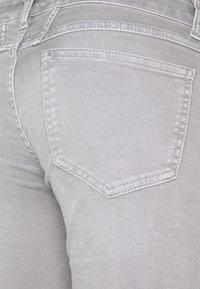 Harmaan farkut, joissa on takatasku, jossa on ommeltu ääriviiva. Sujuva pinta ja tiukka muoto sekä hillityt ompeluyksityiskohdat.