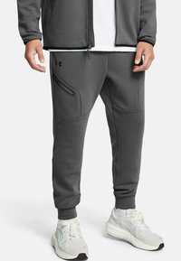 Gray sweatpants made of soft material, featuring a zippered pocket and tapered ankles. Worn with white sneakers for added contrast.