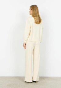 Sada krémovej farby na voľnočasové nosenie, ktorá obsahuje mikinu s voľným strihom a dlhými rukávmi a nohavice so širokými nohavicami. Hladká textúra, minimalistický dizajn, bez viditeľných vzorov.