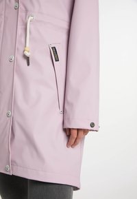 Ljusrosa vattentät jacka med tryckknappar, dragsko huva och sidfickor. Slät textur och figursydd design med silverdetaljer.