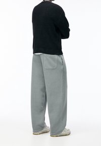 Pull côtelé noir associé à un pantalon gris ample avec une poche arrière. Chaussures de couleur claire. Design simple avec une coupe décontractée.