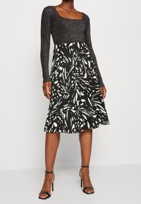 Top de manga larga negro y plateado con purpurina, combinado con una falda negra que presenta patrones abstractos blancos; corsé ajustado y dobladillo acampanado.