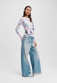 Lilla õlakott musta rihmaga, kantud mitmevärvilise tie-dye pikakäpiga särk ja heledatest sinistest lõdvikutest pükstest.