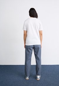 Witte katoenen T-shirt en grijze broek. T-shirt is met korte mouwen en heeft een ronde halslijn. De broek is losvallend met een rechte pasvorm. Zilveren schoenen.