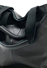 Zwarte leren tote bag met een textuur, voorzien van stevige stoffen handvatten die over de bovenkant lopen en een uniek ontwerp creëren.