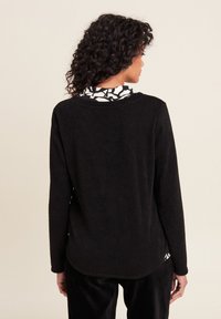 Schwarzer, langärmeliger Pullover mit strukturiertem Strick-Finish. Gerundeter Saum und Rückendetail mit einem weißen grafischen Muster darunter.