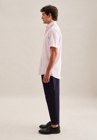 Camicia rosa a maniche corte con colletto, abbinata a pantaloni scuri blu navy e scarpe nere stringate, mostrata di lato.