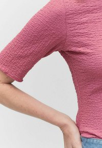 Teksturowana różowa bluzka z krótkim rękawem, charakteryzująca się dopasowanym krojem, widocznymi szwami i lekko postrzępionym dołem, połączona z jasnymi dżinsami.