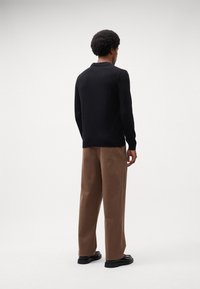 Zwarte gebreide trui met lange mouwen, ontspannen pasvorm, gecombineerd met lichtbruine wijde broek. Gladde textuur, casual ontwerp, minimale details.