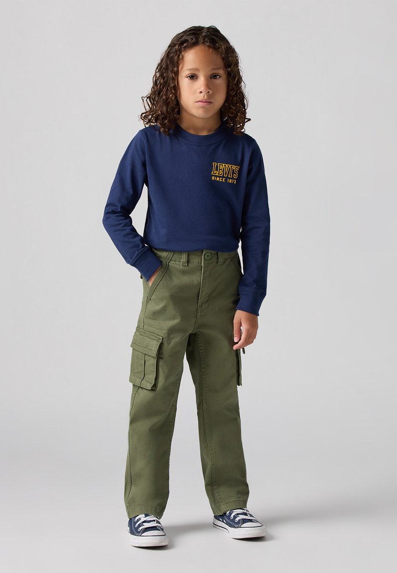 Camicia a maniche lunghe blu navy con logo giallo; pantaloni cargo verde oliva con tasche laterali; sneakers blu con accenti bianchi; design dritto.