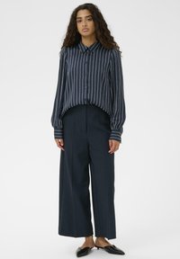 Jūras zilas svītrains pogājams krekls ar plašām piedurknēm, kopā ar tumši jūras zilām platām biksēm ar augstu jostasvietu, papildināts ar melnām dzīvoklēm apaviem.