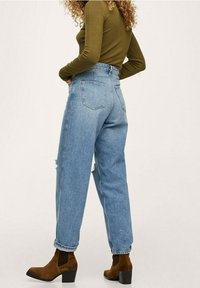 Jean en denim bleu taille haute avec une coupe décontractée, présentant des accents déchirés et des poches arrière, associé à des bottines marron.