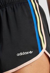 Svarta atletiska shorts med rosa detaljer, med tre färgade sidostrecker i blått, gult och svart, samt en vit Adidas-logotyp.