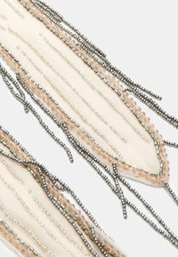 Accessoire perlé composé de perles argentées et rose clair, disposées en motif linéaire sur une base en tissu pâle, avec des textures et des longueurs variées.