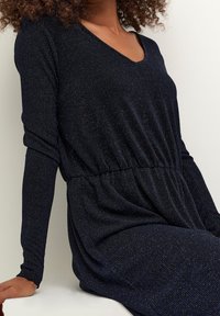 Dlouhé rukávy námořnicky modré šaty s výstřihem do V, které mají řasený pas a jemnou metalickou nit pro strukturovaný vzhled.