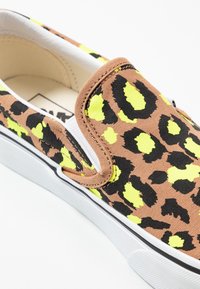 Sneakers slip-on con tomaia in canvas marrone con stampa leopardata nera e gialla neon. Suola in gomma bianca con una linea di accento nera.