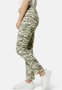 Hoge taille, strakke broek in een gestructureerd, wit en bruin zebra-patroon met zijspleten bij de enkels, gecombineerd met witte sneakers.