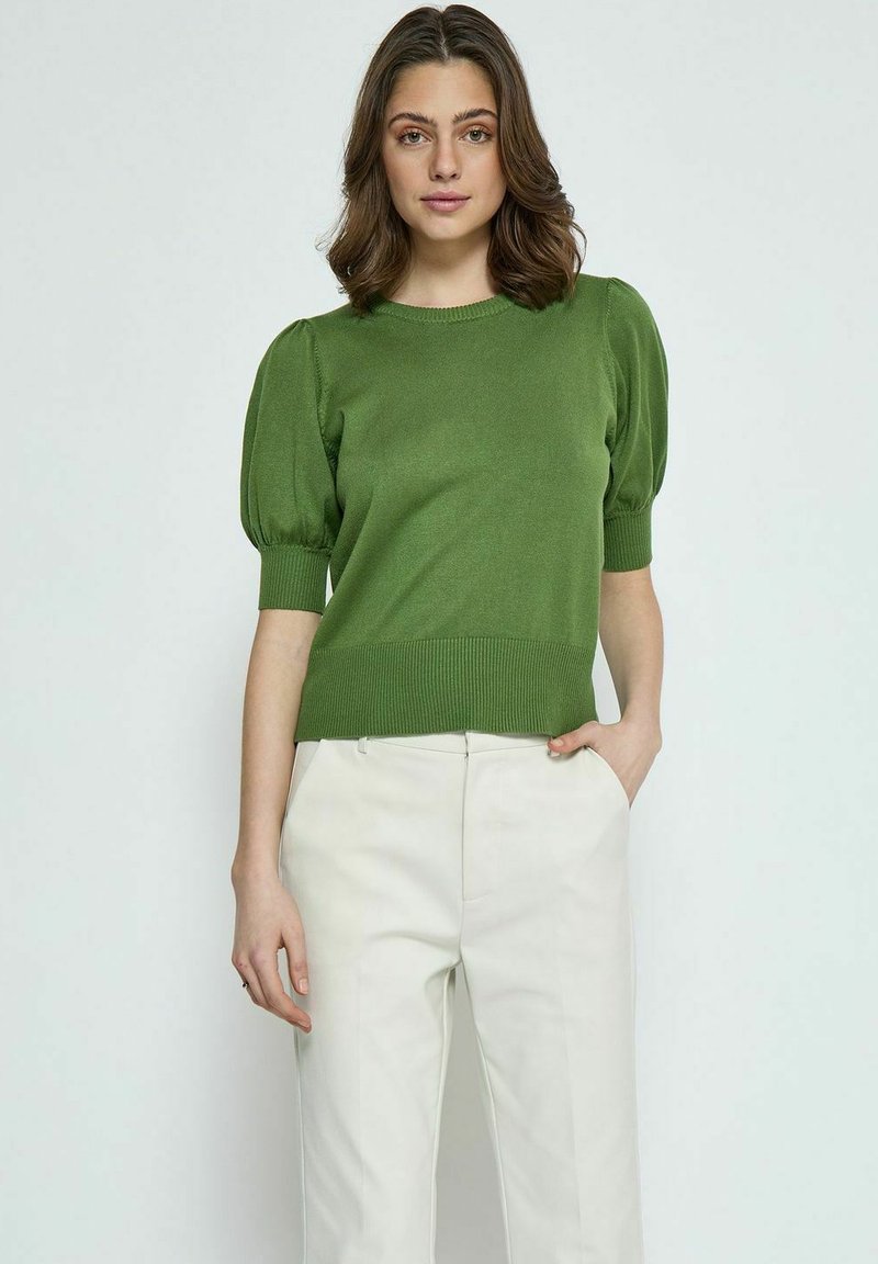 Maglione verde a maglia con maniche a sbuffo corte, orlo e polsini a costine, abbinato a pantaloni color crema. La texture appare liscia e morbida.