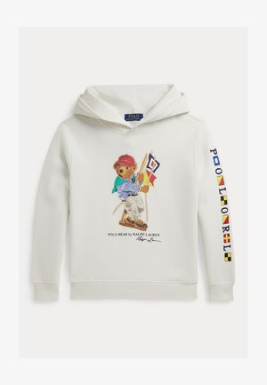 Balta kapuce ar Polo lāci, kurš valkā sarkanu cepuri, zaļu šalli, svītrainu kreklu un tur rokās jūras karodziņus; Polo Ralph Lauren logo uz piedurknes.