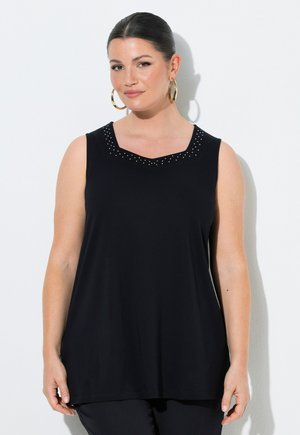 Kvinde med mørkt hår i en glat knold iført guldringøreringe og en sort ærmeløs top med små nitter rundt om halsudskæringen.