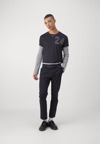 Chemise courte à manches avec des manches longues rayées de couleur marine, en tissu jersey, col rond, numérotation « 24 » à l'avant, associée à un pantalon sombre et des chaussures.