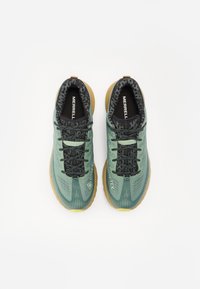 Green and black hiking shoes with a textured upper, patterned laces, and a brown rubber sole. GORE-TEX branding visible on the side.