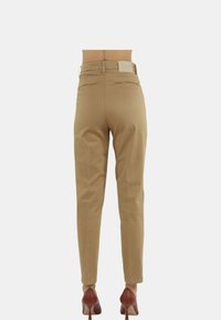 Pantaloni beige con una vestibilità slim, dotati di tasche posteriori con una leggera cucitura decorativa e un'etichetta del marchio sulla cintura. Indossati con tacchi marroni.
