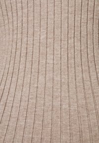 Tissu côtelé beige avec une texture douce, présentant des lignes verticales et un motif en tricot, adapté pour les vêtements ou le rembourrage.