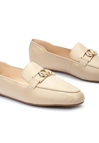 Mocasines de cuero beige con punta afilada, con una hebilla de acento en tono dorado y costuras mínimas. Acabado suave y suela flexible.