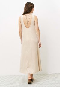 Langes, rückenfreies Kleid in hellem Beige mit strukturierter Oberfläche. Verfügt über eine Halter-Träger und ein fließendes, bodenlanges Design.