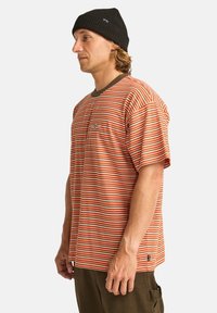 Stripet kortærmet t-shirt i orange og creme, med en mørkebrun halsudskæring og et lille logo på brystet. Tekstureret bomuldsstof.