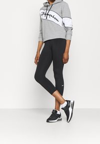 Felpa corta grigia con accenti neri e bianchi, abbinata a leggings neri attillati e scarpe da ginnastica nere con un logo bianco.