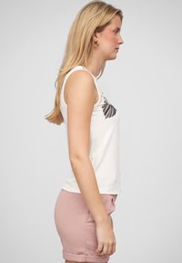 Débardeur blanc léger avec une texture côtelée, arborant un graphique de plumes noires sur la poitrine. Associé à un short rose.