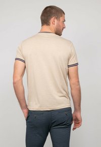 T-shirt beige à manches courtes avec un col et des manches bordés de marine, fabriqué en matériau doux, porté avec un pantalon bleu foncé texturé.