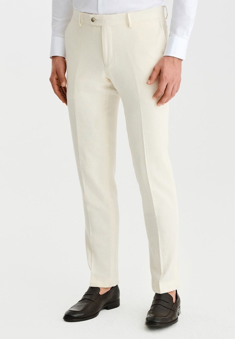 Kremowe spodnie wykonane z lekkiego materiału, o dopasowanym kroju, gładkiej fakturze i zapięciu na jeden guzik. Zestawione z ciemnymi mokasynami.