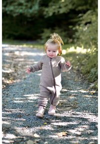 Hnědý vlněný overal s předním zipem a žebrovanými manžetami, který nosí dítě kráčející po štěrkové cestě obklopené zelení.