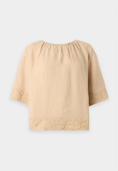 Blouse beige à manches courtes avec encolure froncée et broderie décorative en boucle le long des manches et de l'ourlet sur fond uni.