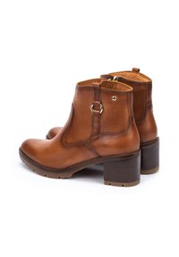 Botas de tobillo de cuero marrón con puntera redondeada, elástico lateral y un tacón corto tipo bloque. Presenta una cremallera trasera y un acento decorativo en forma de anillo.